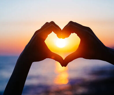 hands forming a heart shape with sunset silhouette. Copy space text.
